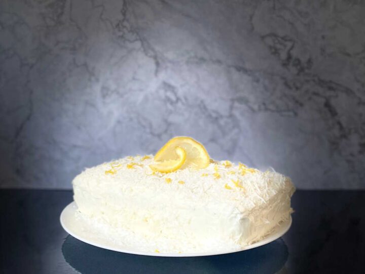 lemon coconut loaf cake garnished with a slice of lemon on a black counter top with a marble background