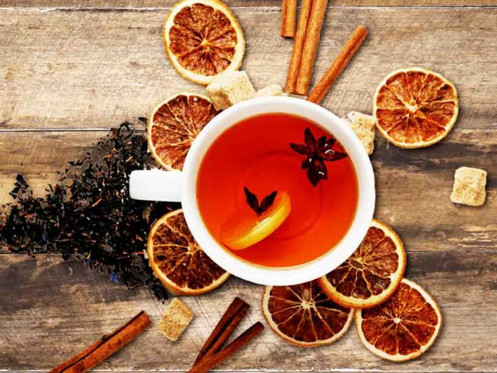 Cinnamon spice tea in a white cup on a wooden table surrounded with orange slices and cinnamon sticks