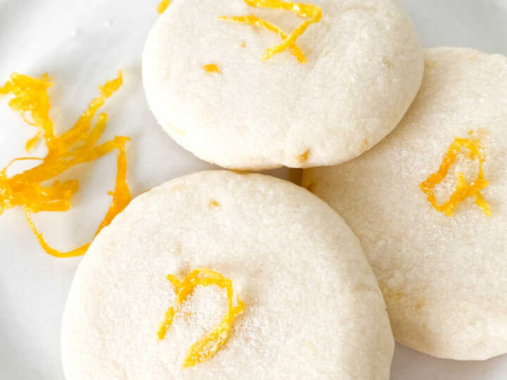 Close up of lemon shortbread cookies and lemon zest on a white plate.