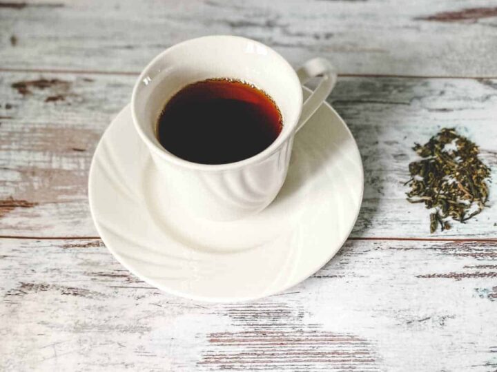 A white cup and saucer containing orange pekoe black tea with tea leaves scattered on a wooden background.
