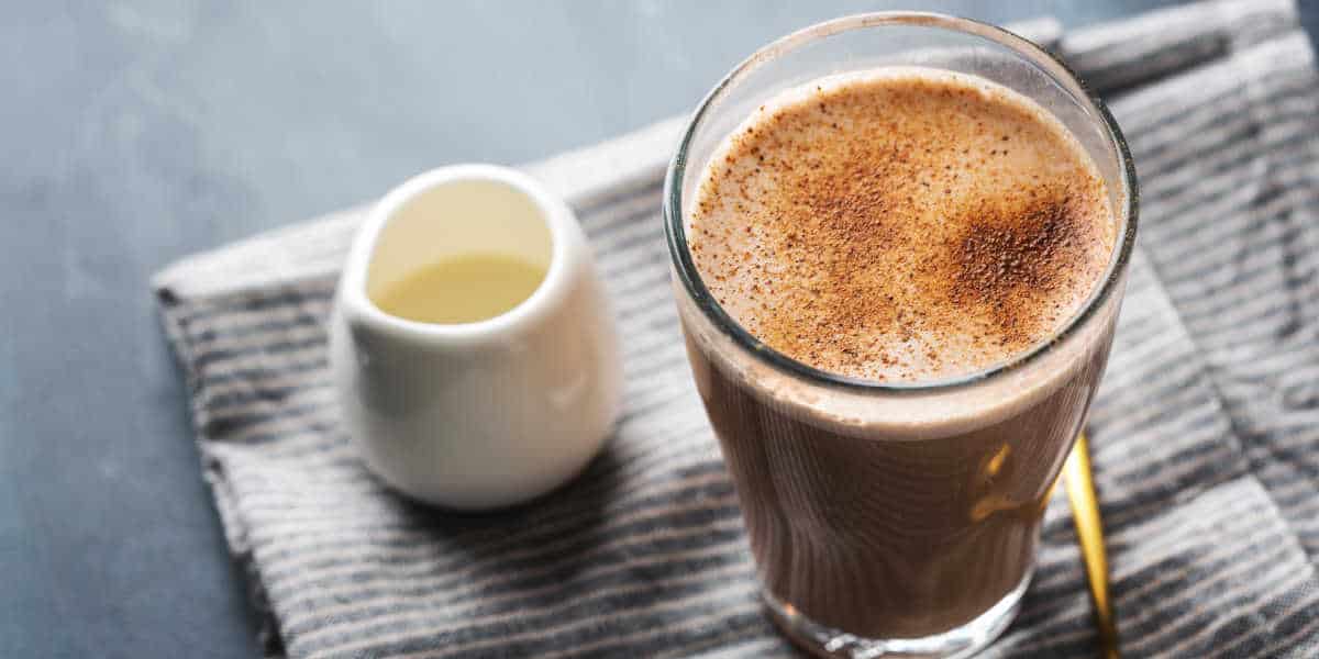 Chai tea latte in a glass on a blue napkin with a white jug of milk.