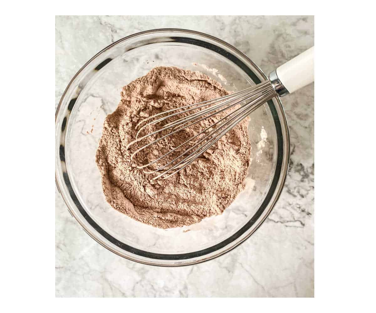 Glass bowl with whisk containing dry ingredients for chocolate cupcakes.