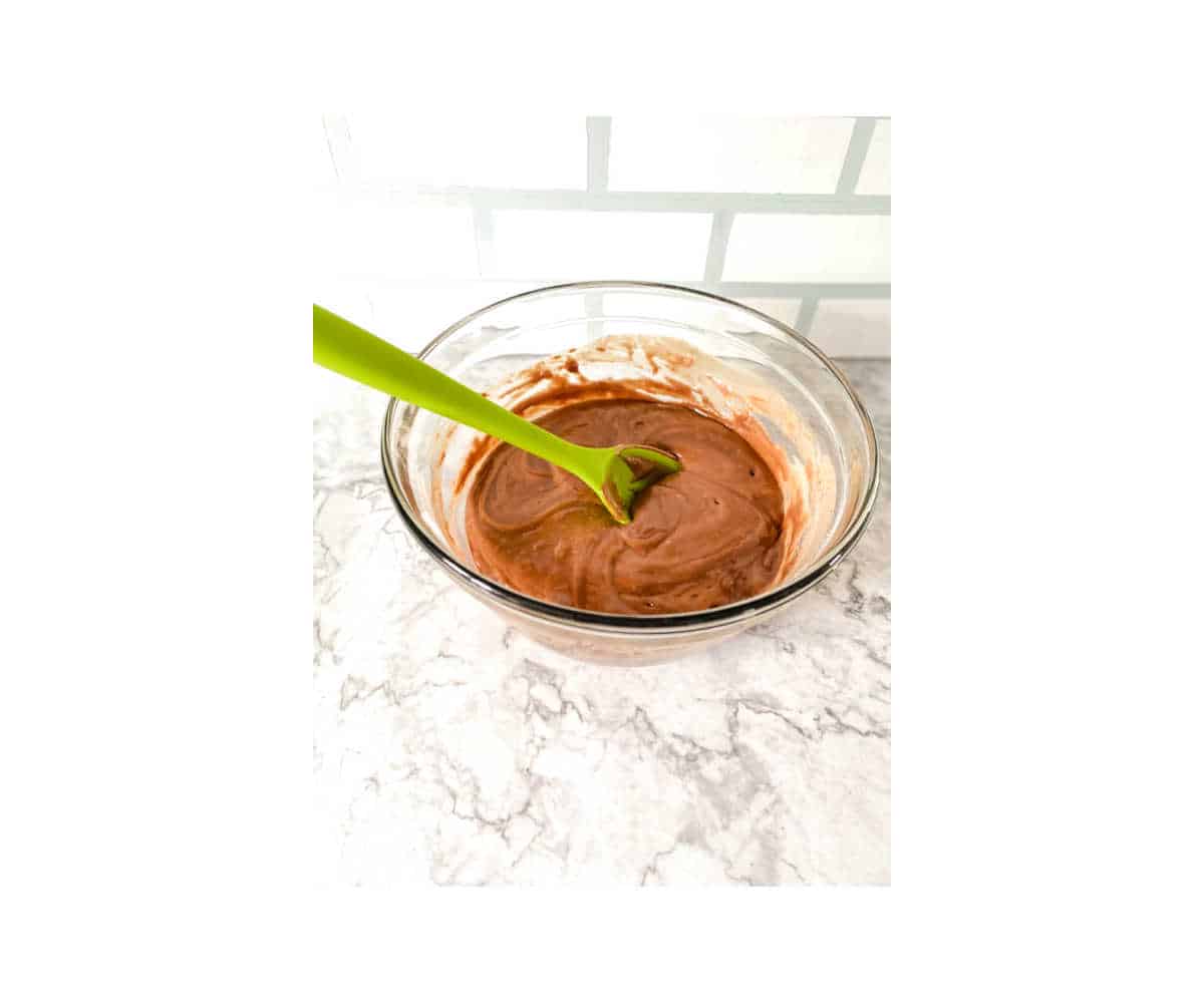 A glass bowl full of chocolate cupcake batter with a green spoon.
