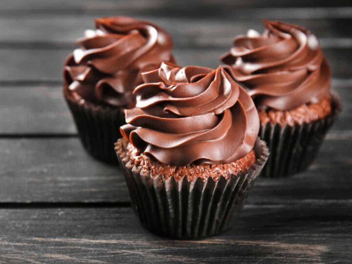 Three cupcakes with chocolate frosting on a wooden background.