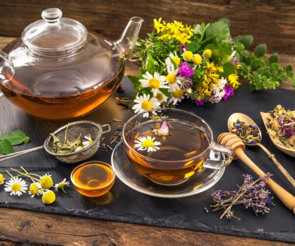 A cup of lavender chamomile tea with fresh chamomile and lavender flowers on a black slate background.