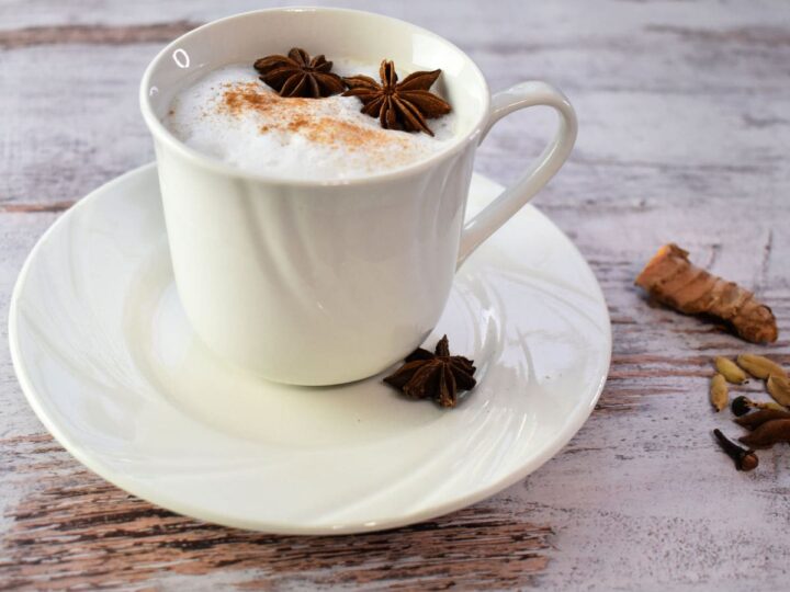 Golden Chai Latte in a white cup on a wooden table with spices scattered around.