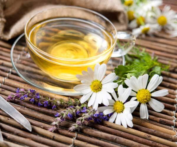 Cup of herbal lavender and chamomile tea with chamomile and lavender flowers on wooden background.