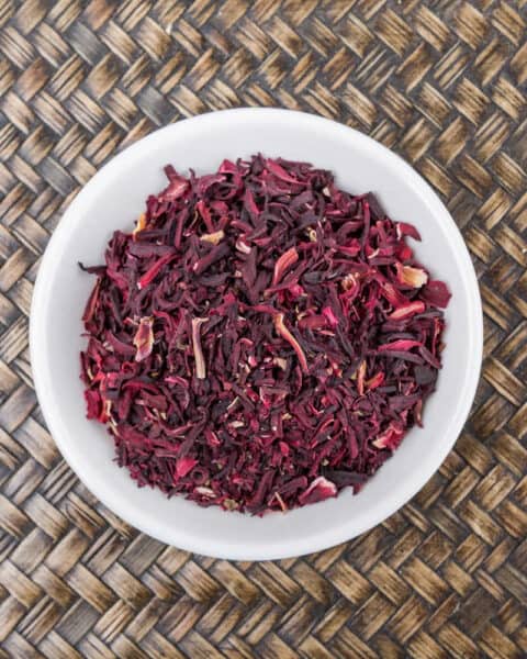 Dried hibiscus flowers in a white bowl on a rattan background.