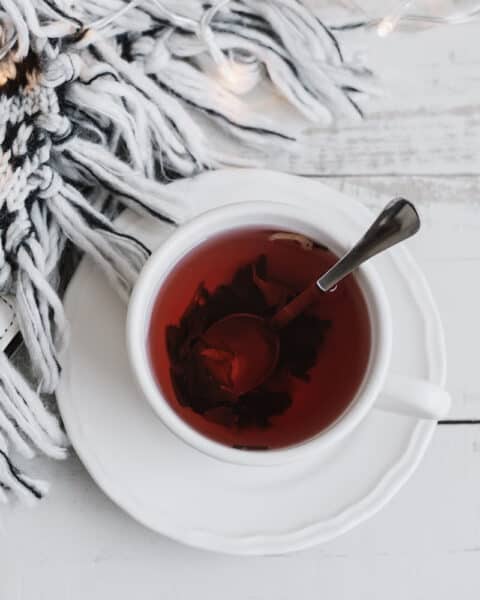 A white cup and saucer containing hibiscus rose hip tea and a spoon on a white wooden background