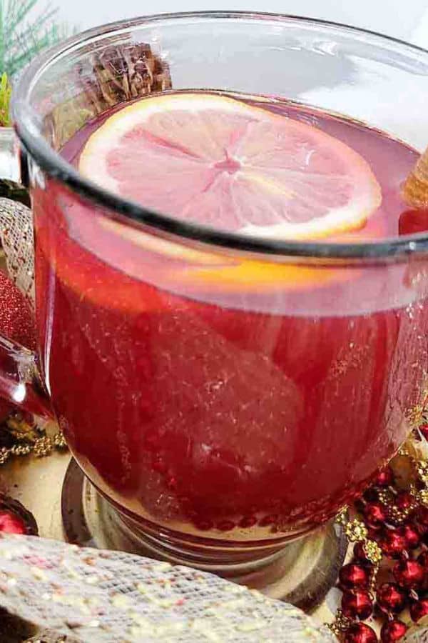 A glass cup containing cranberry tea and an orange slice surrounded by Christmas ribbon and beads.