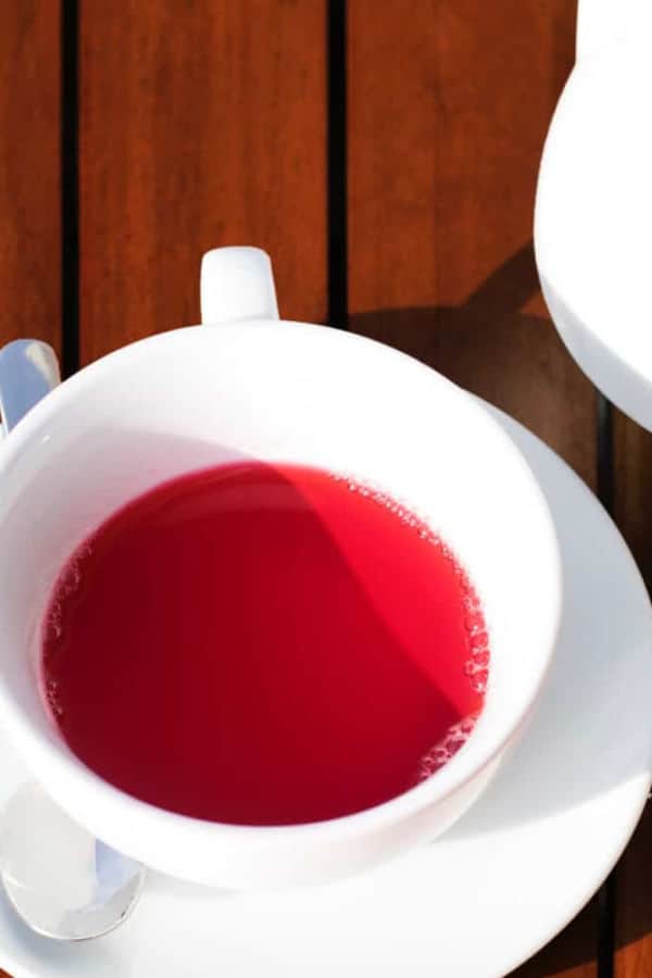 A white cup and saucer containing hibiscus rose tea.