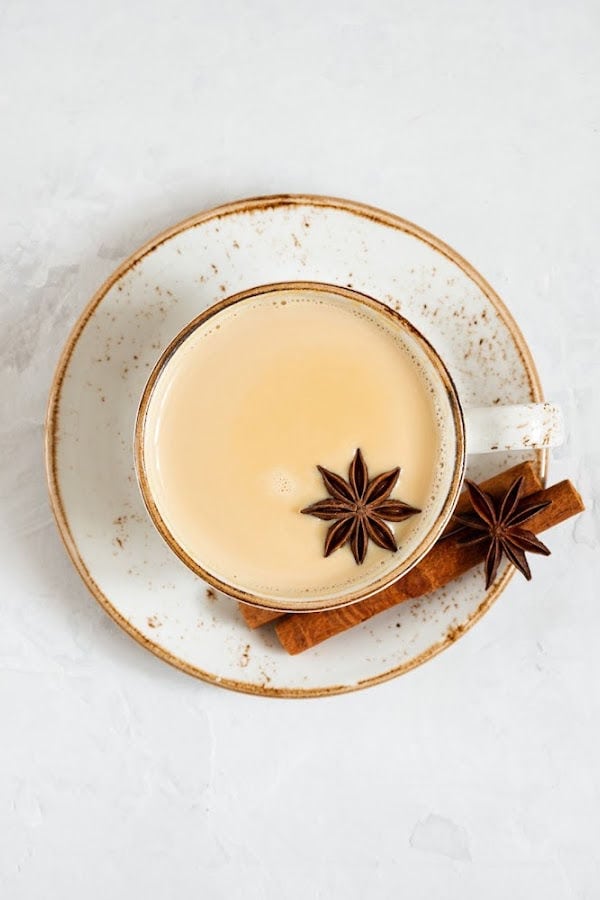 A brown and white cup and saucer containing chai tea with star anise and cinnamon sticks on a white background.