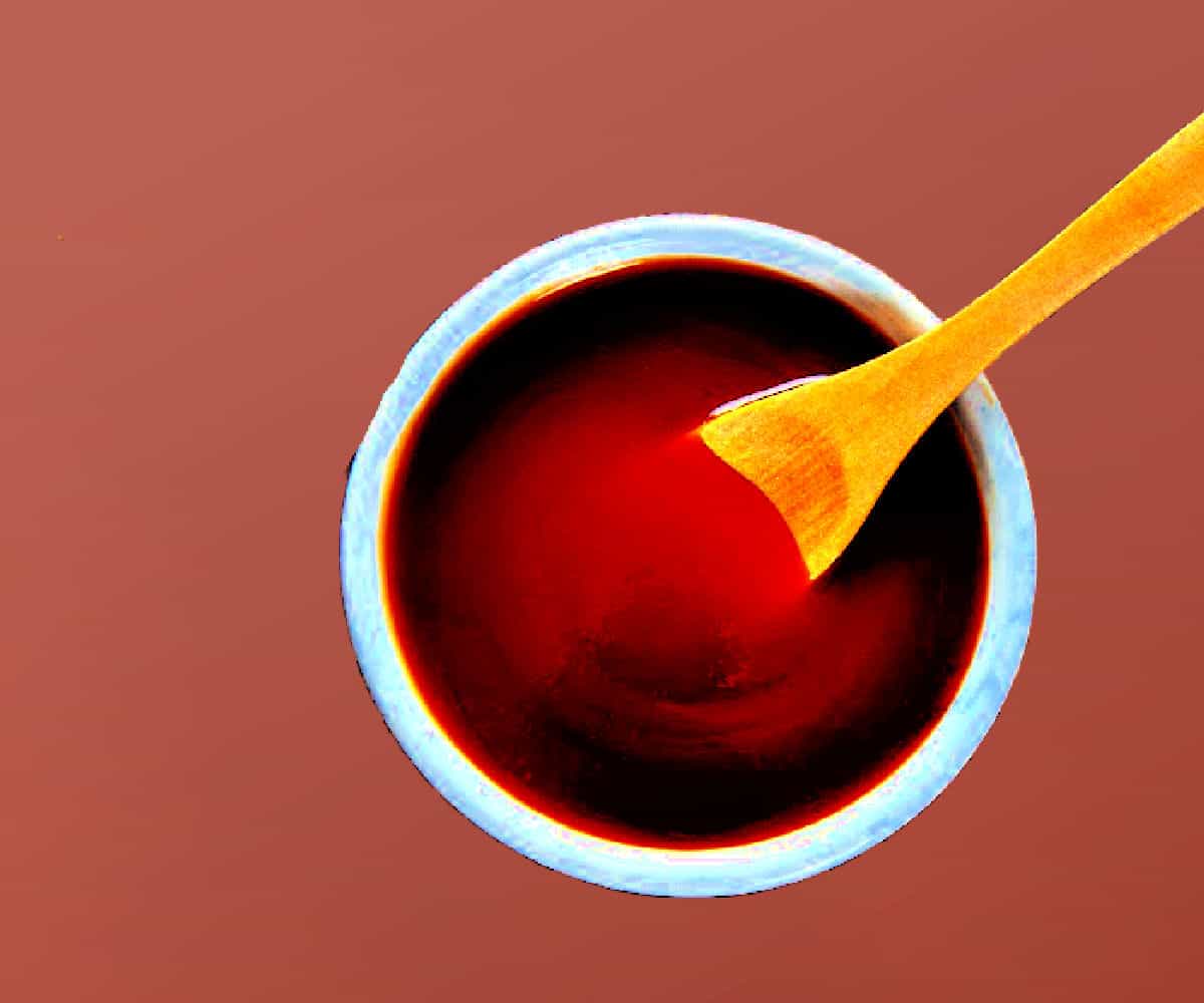 Rose hip syrup in a white bowl with a wooden spoon on a red background.