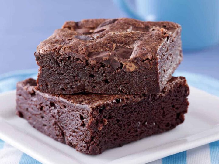 Two fudge brownies on a white plate sitting on a blue and white striped napkin.