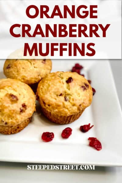 Orange cranberry muffins on a white plate surrounded with dried cranberries. The text reads orange cranberry muffins. steepedstreet.com