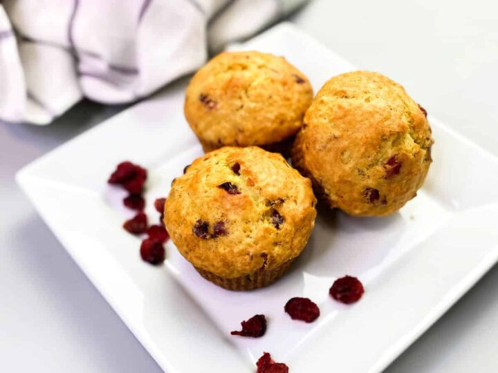 Orange cranberry muffins on a white plate surrounded with dried cranberries.