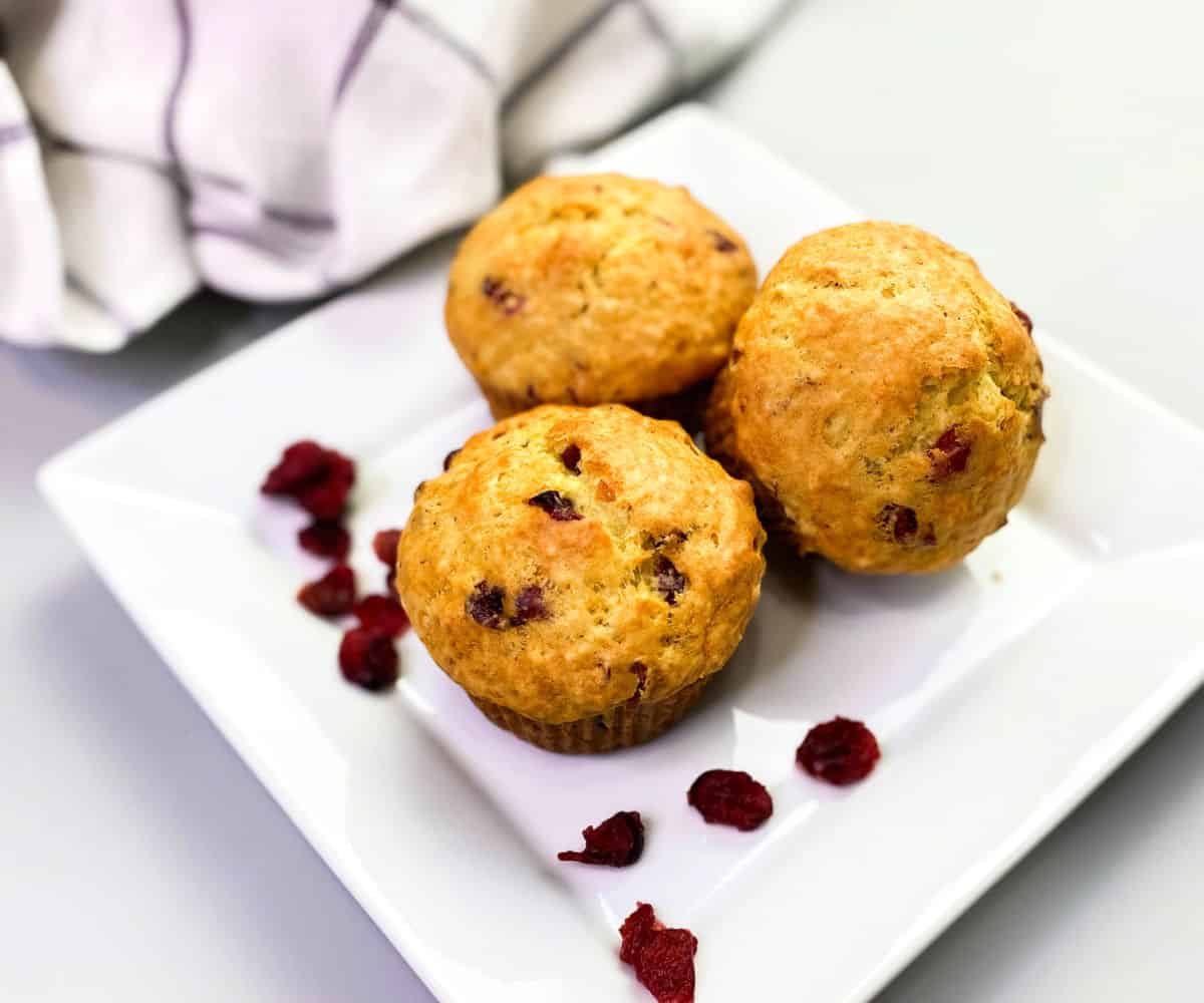 Orange cranberry muffins on a white plate surrounded with dried cranberries.