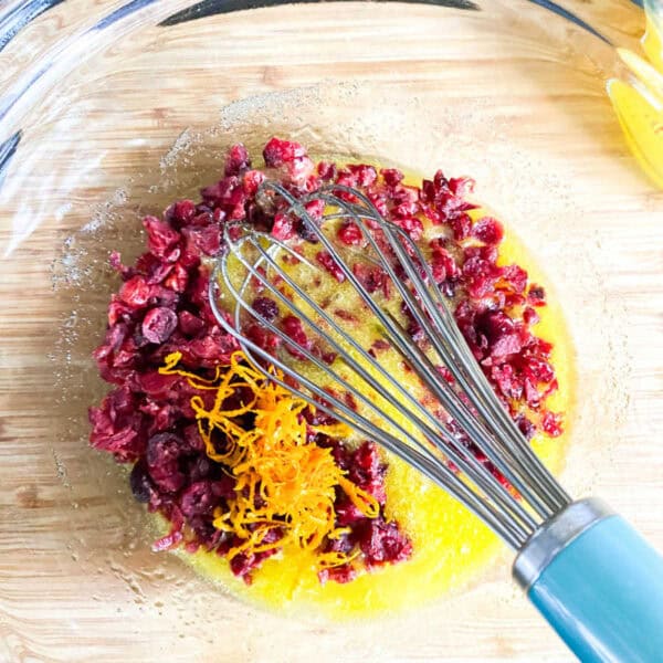 Dried cranberries, orange zest, and eggs in a bowl with a whisk.