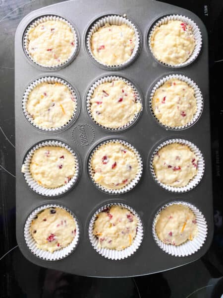 Orange cranberry muffin batter in a muffin tin.