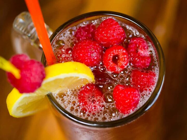A glass of raspberry iced tea with raspberries and a lemon slice.