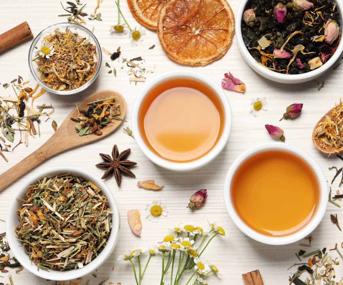 Various dried flowers and herbs on a table with cups of herbal tea.