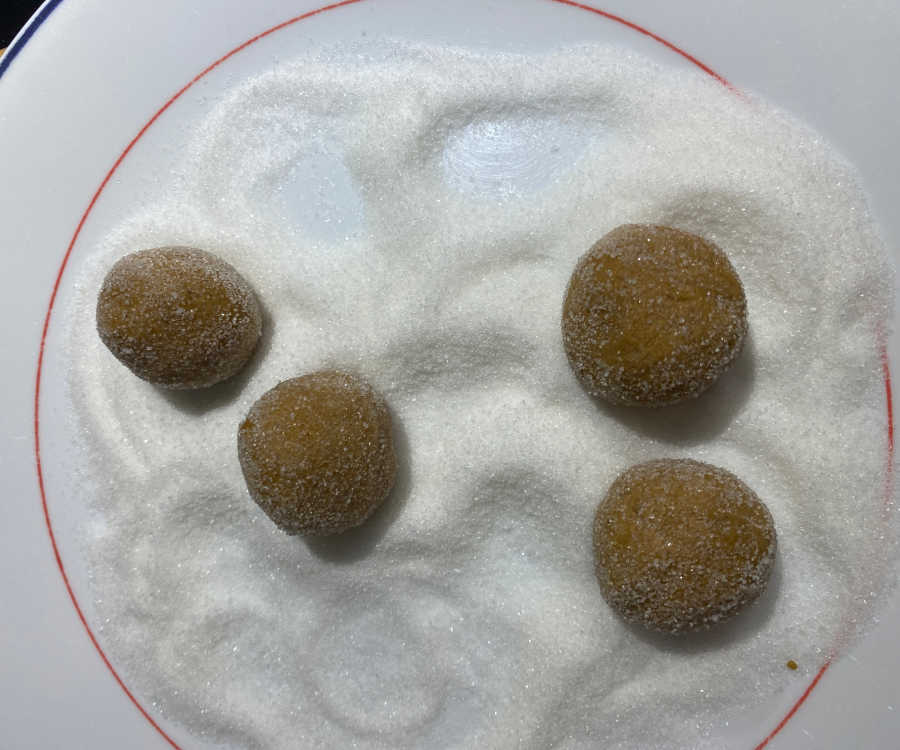 Ginger snap cookies being rolled in sugar.