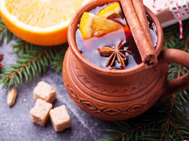 A brown stone ware mug containing Christmas tea with cinnamon sticks, star anise, and orange slices.