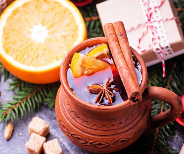 A brown stone ware mug containing Christmas tea with cinnamon sticks, star anise, and orange slices.