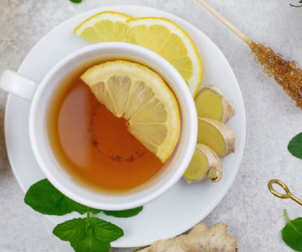 Ginger tea in a white teacup and saucer surrounded by ginger and mint.