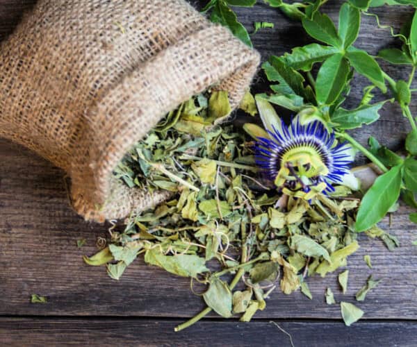 Passion flower and leaves spilling out of a small burlap bag on a wooden table.