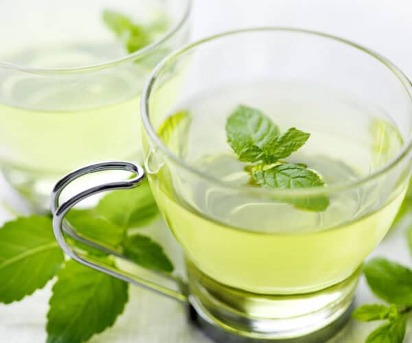 Peppermint tea in a glass cup with peppermint leaves.