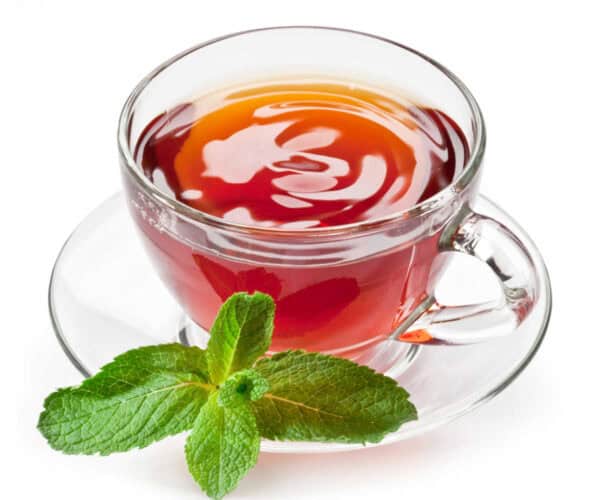 Mint tea in a glass cup and saucer with a mint leaf on a white background.