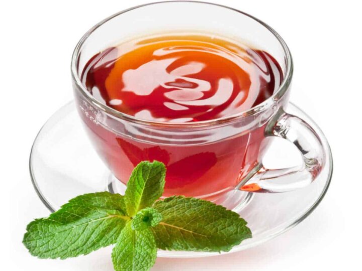Mint tea in a glass cup and saucer with a mint leaf on a white background.