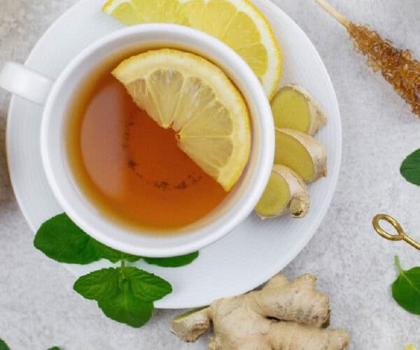 Ginger tea in a white teacup and saucer with ginger root and lemon slices.