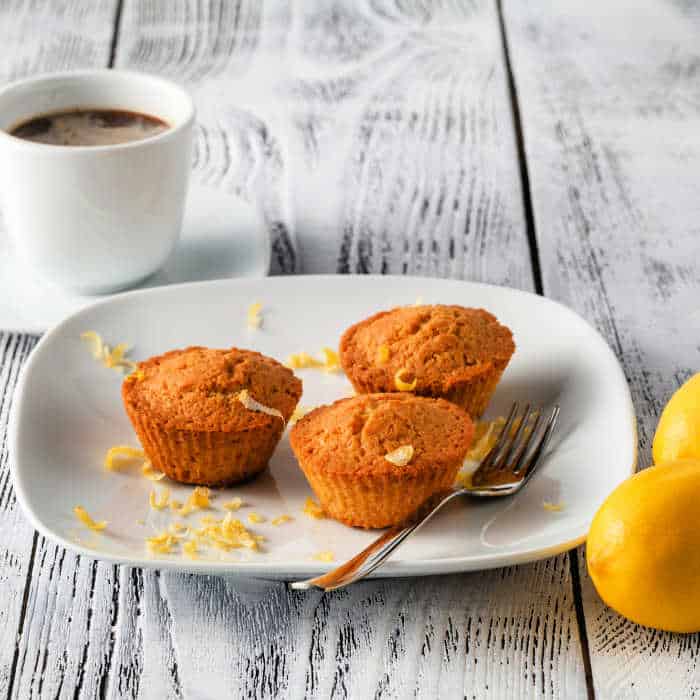 Three muffins on a white plate with a cup of tea and lemons.