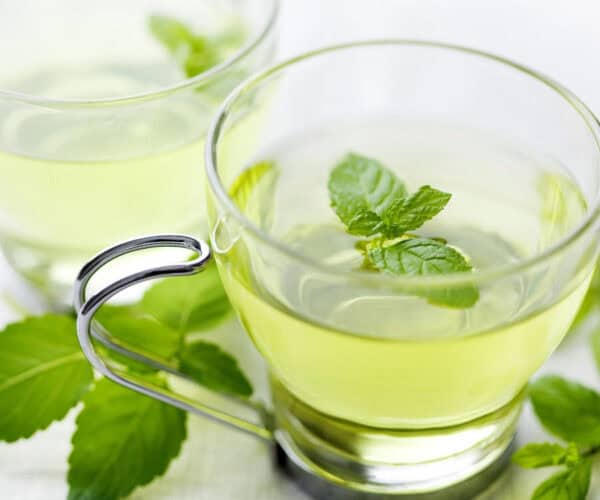 Peppermint tea in a glass cup with peppermint leaves.