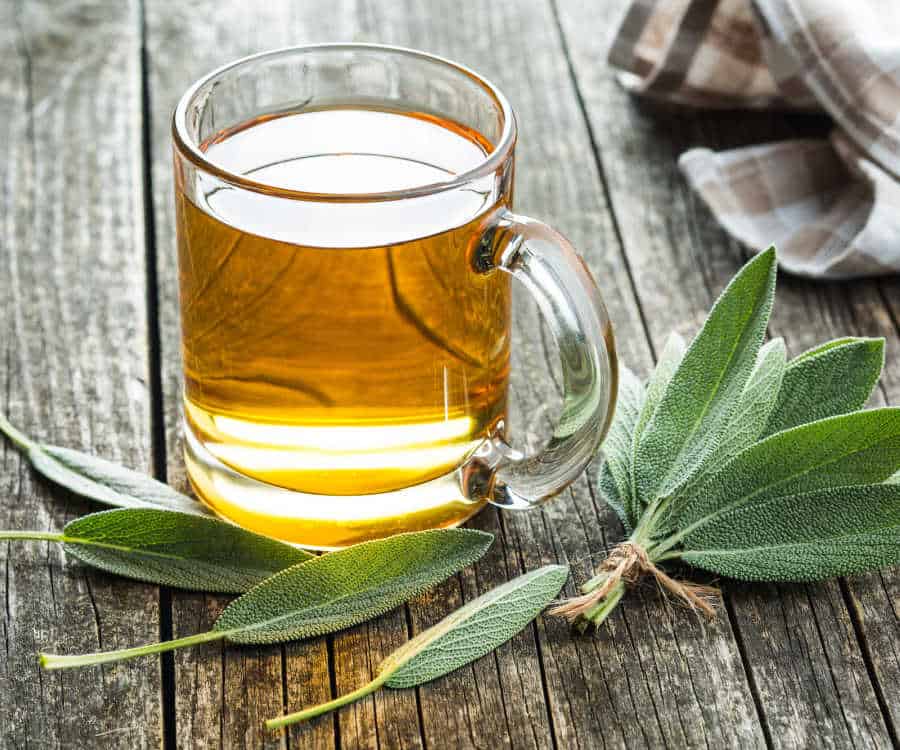 Sage tea in a glass mug on a wooden table with sage leaves.