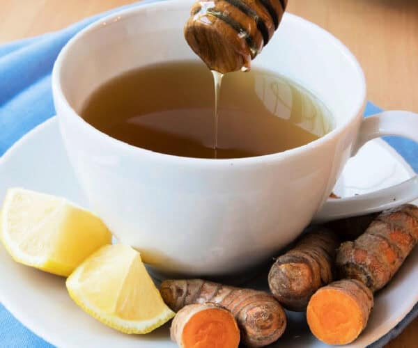 Turmeric tea in a white teacup and saucer with turmeric roots and lemon wedges.