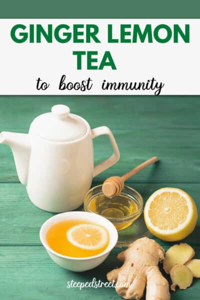 A white teapot and cup with ginger lemon tea and a bowl of honey, a lemon and a piece of ginger on a green wooden background. The text reads ginger lemon tea to boost immunity.
