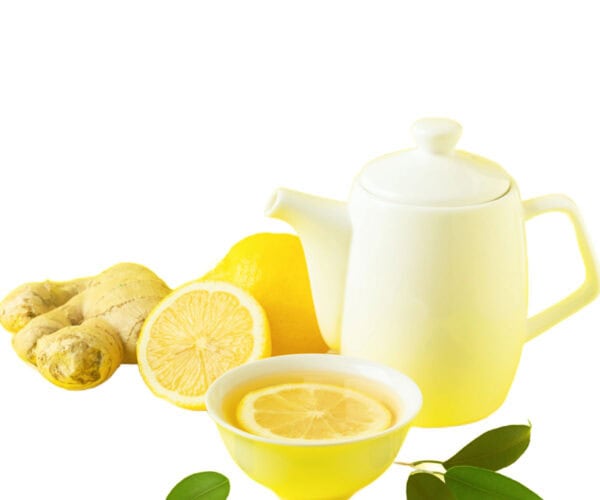 A white teapot and cup with ginger lemon tea and a lemon and a piece of ginger on a white background.