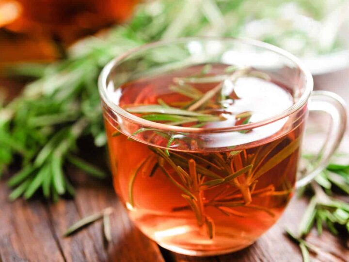 Rosemary tea in a glass cup and fresh rosemary sprigs.