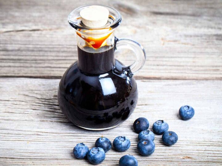 A glass bottle of blueberry syrup and fresh blueberries on a wooden board.