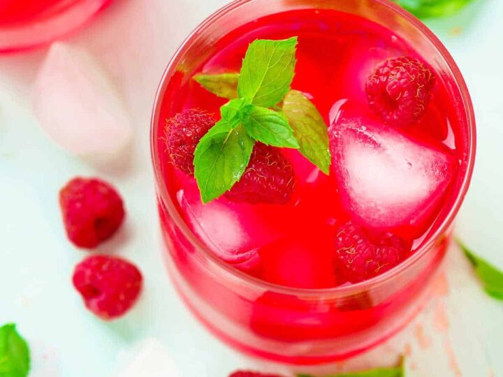 Iced raspberry and mint tea in a glass with raspberries and mint.