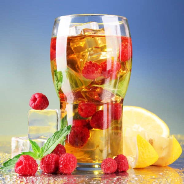 Iced raspberry and mint tea in a glass with raspberries and mint.