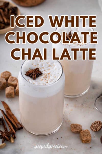 Two iced chai latte in glass cups with cinnamon, sugar cubes and star anise on a marble table. The text reads iced white chocolate chai latte.