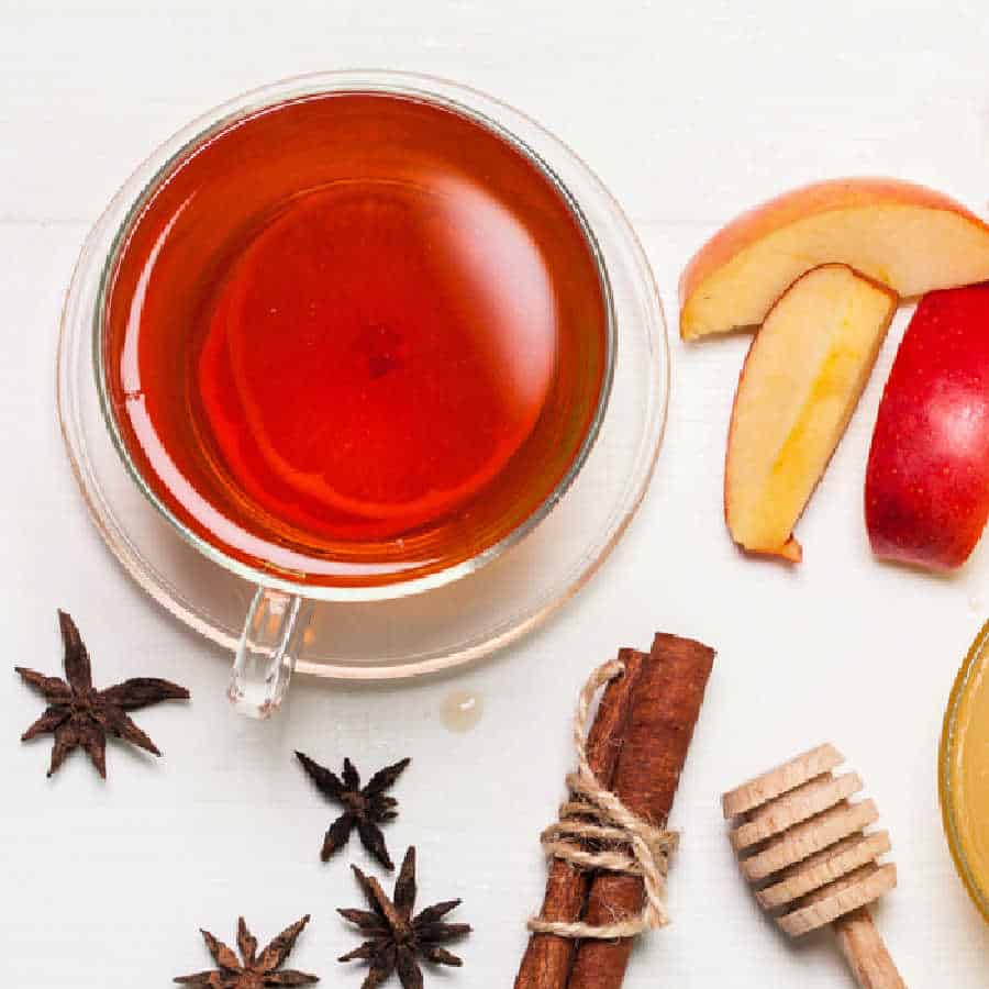 Cinnamon tea in a glass cup with spices and apple slices.