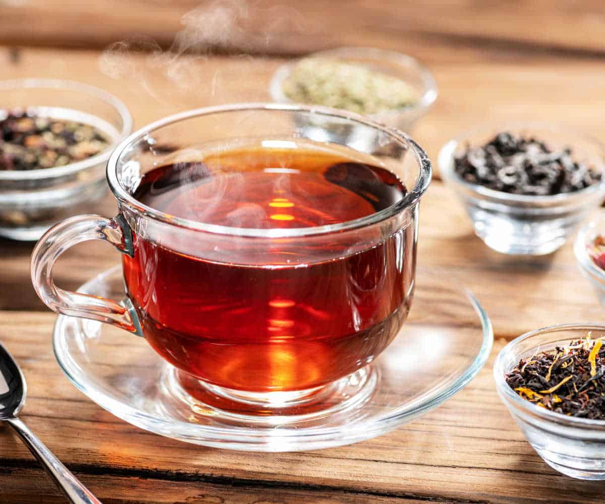 Herbal tea in a glass cup surrounded by glass dishes of various herbs.