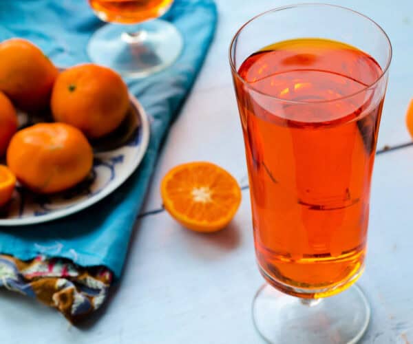 Tangerine tea in a tall glass with fresh tangerines on a blue napkin.