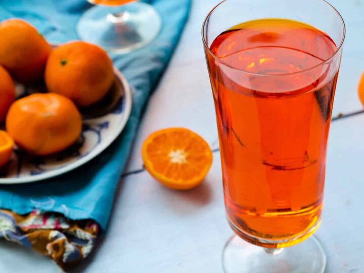 Tangerine tea in a tall glass with fresh tangerines on a blue napkin.