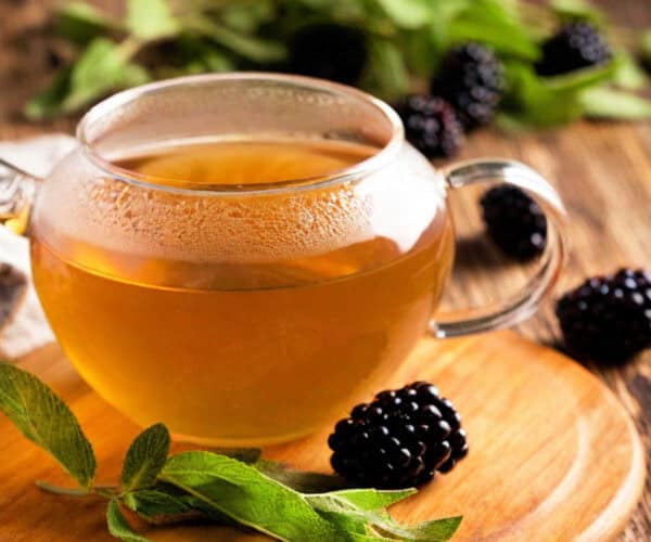 Blackberry sage tea in a glass pot with blackberries and sage leaves.